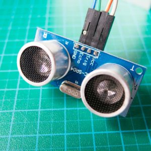 HC-SR04 ultrasonic distance sensor module with connecting wires on a blue circuit board, placed on a green grid mat.