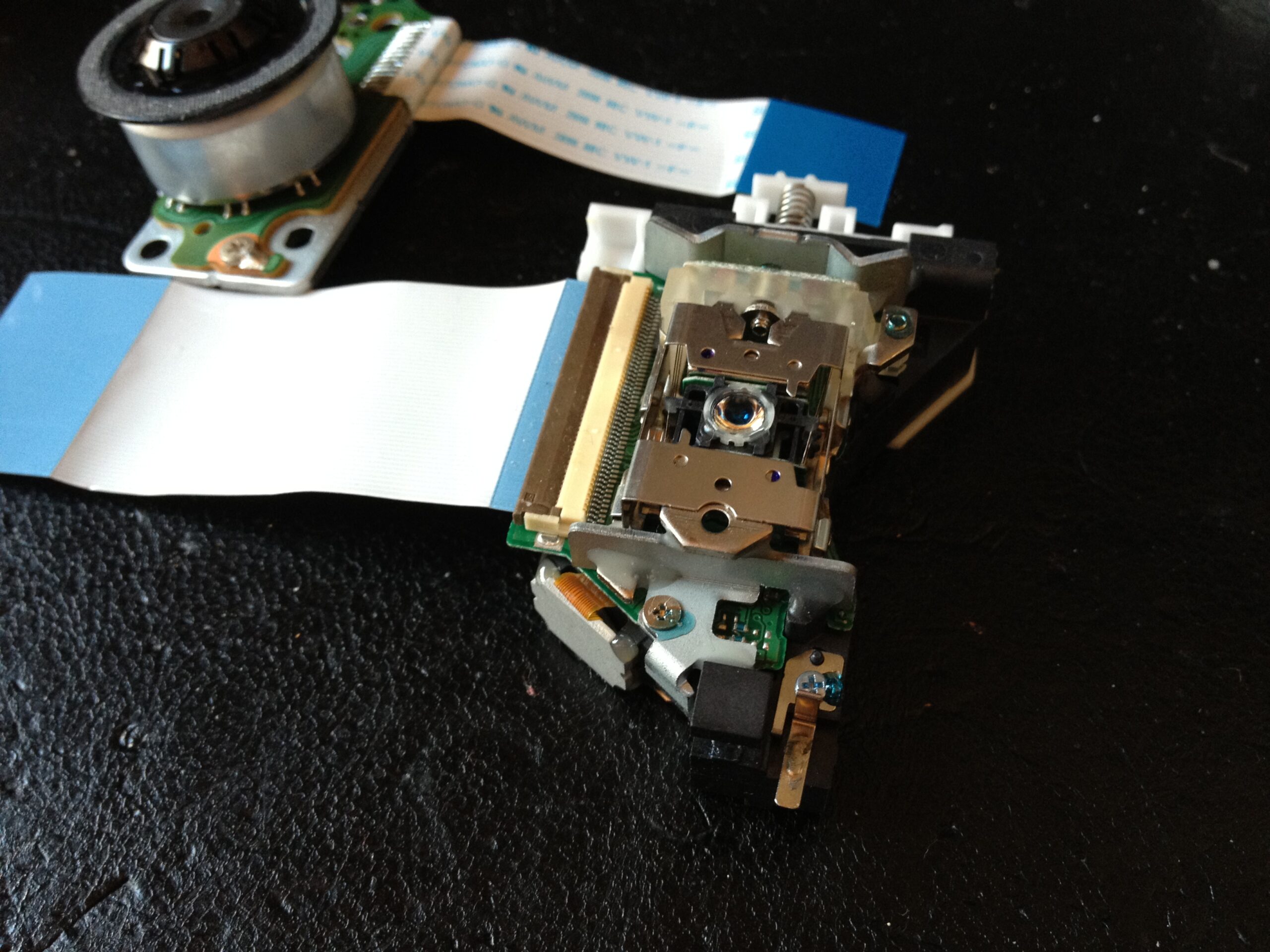 Close-up of the laser optical unit detached from the sled rails, with the collimating lens visible